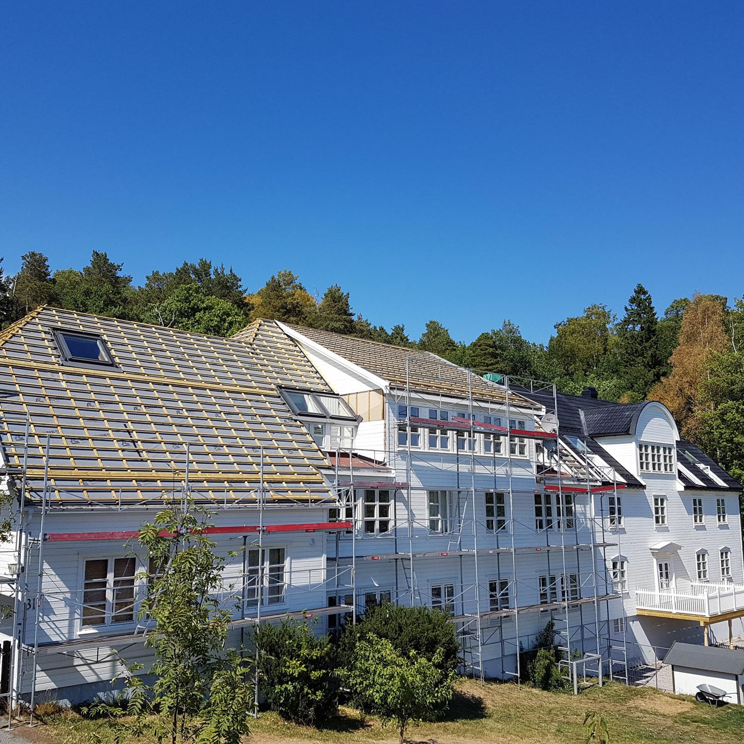 Stort hvitt bygg med nytt tak og stillas