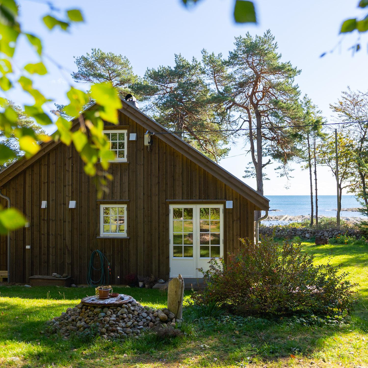 Nytt feriehus i grånet trekledning mellom furutrær, med sjøen bak, på Bjellandstrand, Tromøy