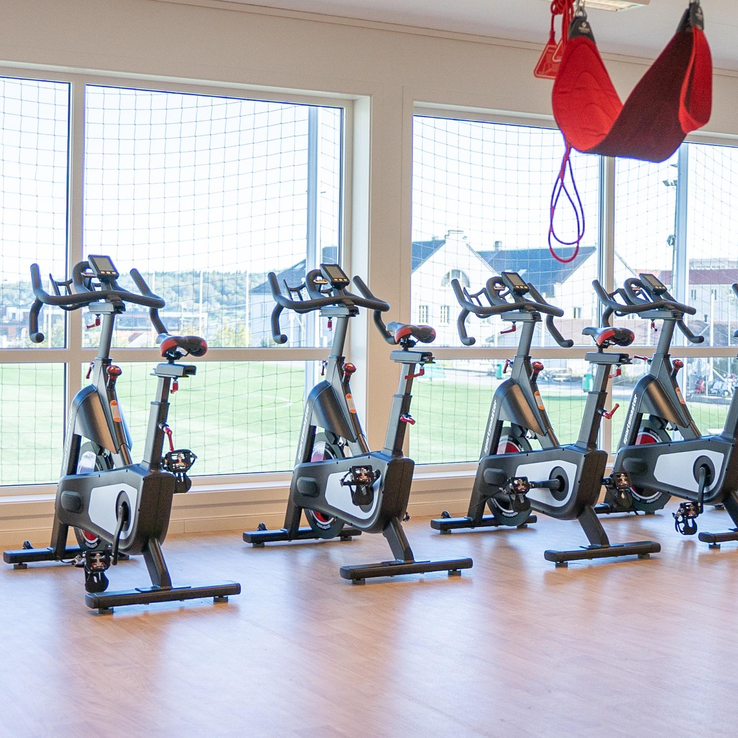 Lyst treningsrom med spinningsykler foran store vinduer