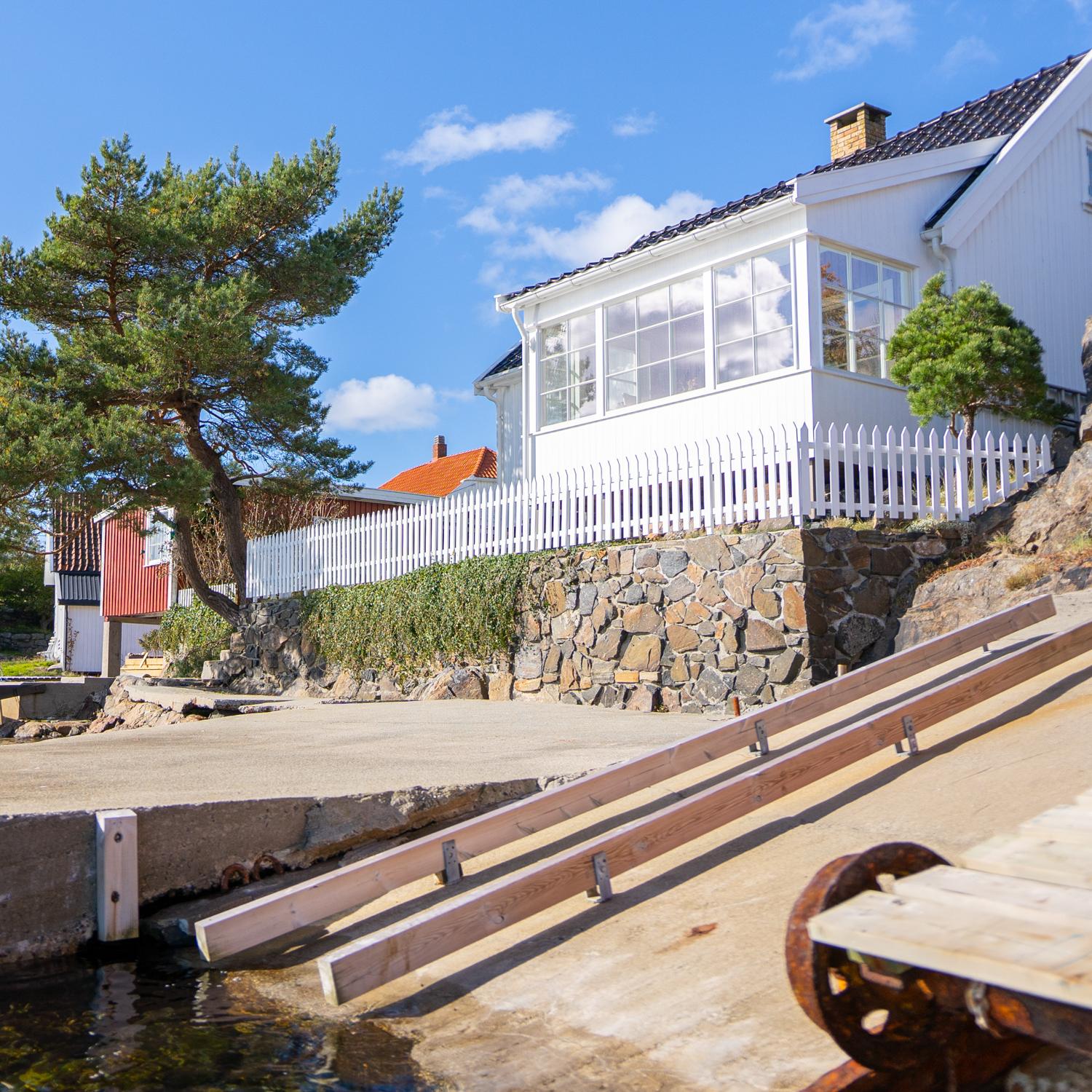 Hvitt hus med glassveranda og hvitt stakittgjerde på en steinmur